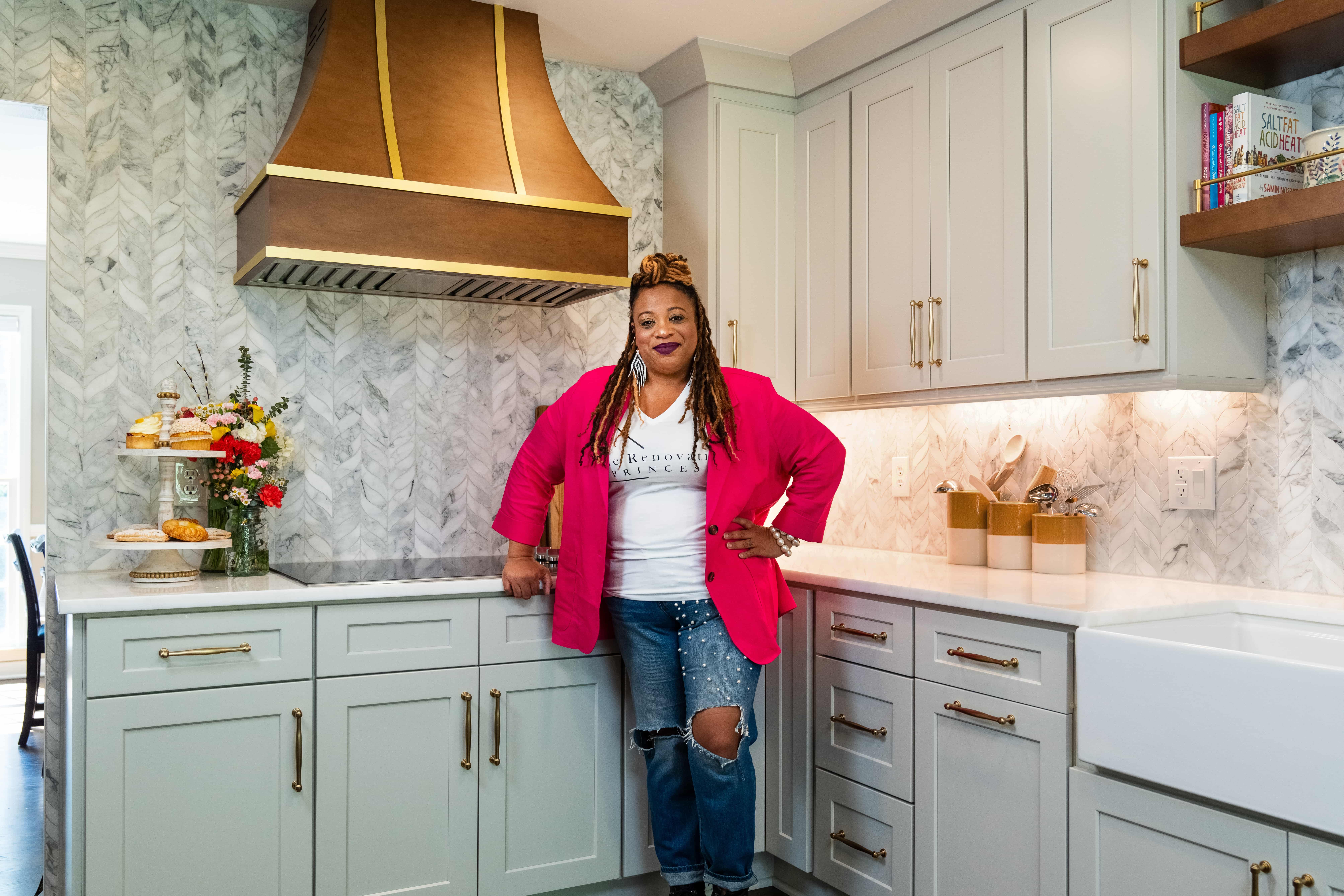 Princess Thompson, Owner of The Renovation Princess standing in a modern, french inspired kitchen with a stained Hoodsly range hood with brass strapping.